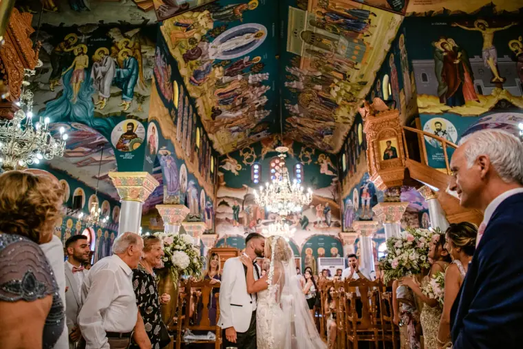 Couple at the altar of an Orthodox church covered in painted icons, guests watching