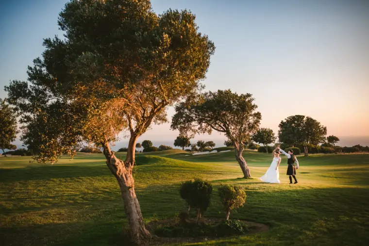 Couple dancing on a golf course lawn among trees in soft evening light