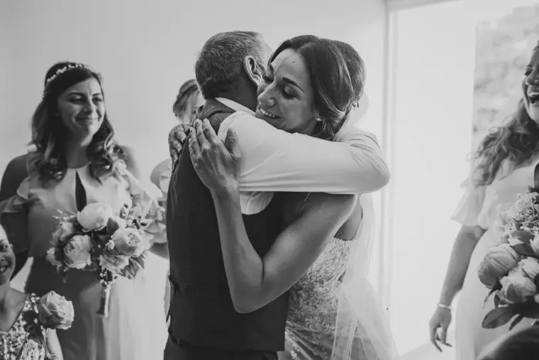 Black-and-white photo of the bride hugging a man as bridesmaids smile nearby
