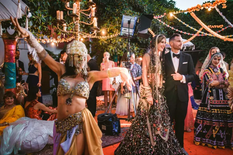 Belly dancer performing for a couple in Indian wedding attire beneath festoon lights