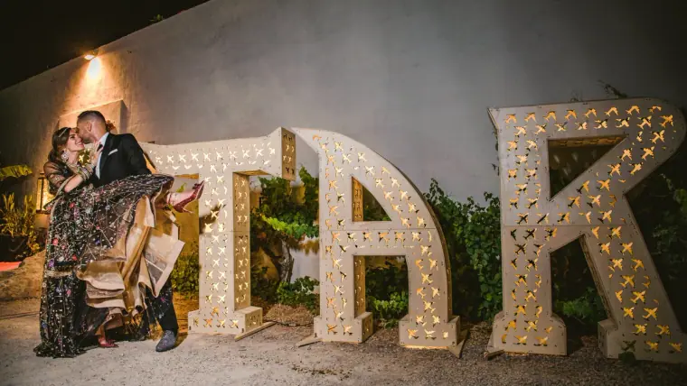 Couple kissing beside giant light-up letters at an evening reception