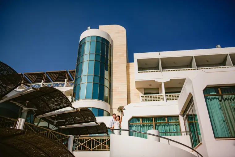 Couple on a balcony of a white hotel with a glass tower under blue sky
