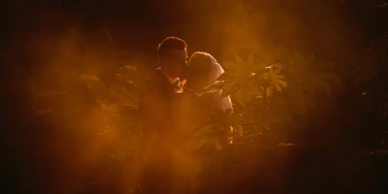 Couple kissing, glimpsed through blurred amber foliage in warm low light
