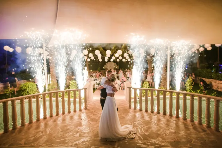 Couple's first dance on a balustraded terrace as cold sparklers erupt behind them