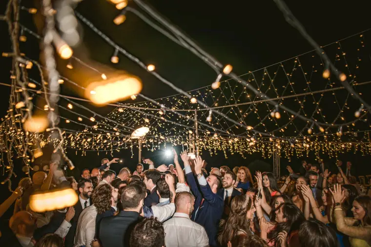 Guests dancing with arms raised beneath a canopy of fairy lights at night