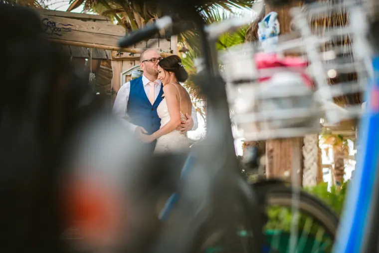 Groom in a waistcoat embracing his bride, framed by a blurred bicycle basket