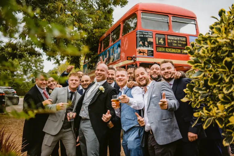 Groomsmen raising pints in front of a red vintage double-decker bus