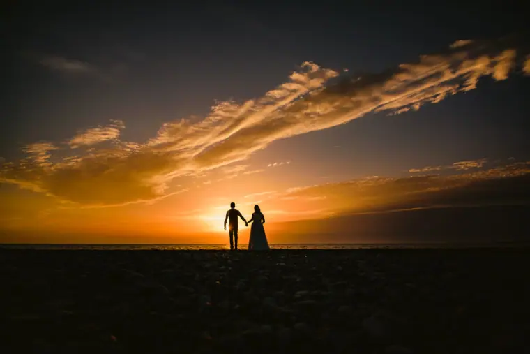 Silhouetted couple holding hands on a horizon beneath a vivid sunset sky