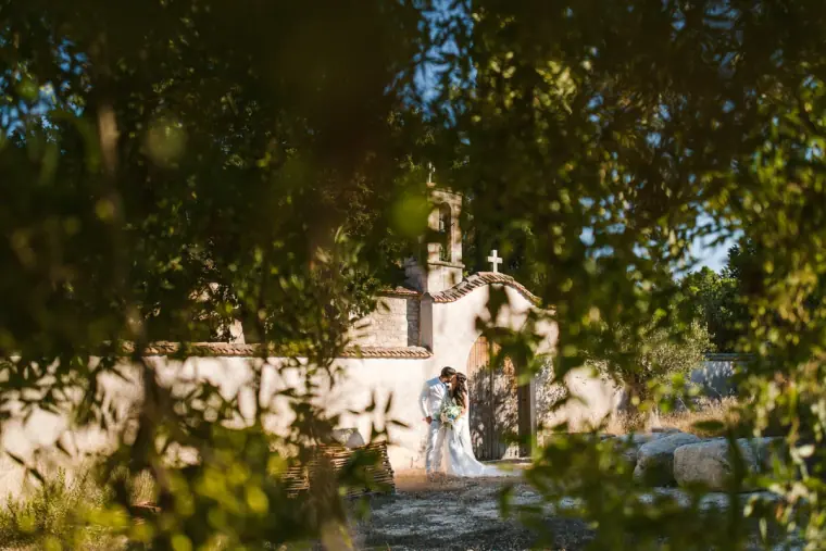 Couple outside a small white chapel, framed by dark overhanging foliage