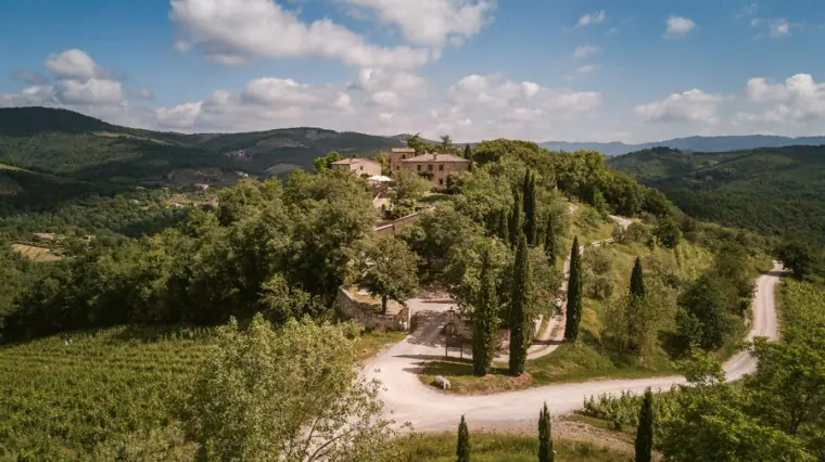 Aerial view of a hilltop villa among cypress-lined drives and rolling green hills