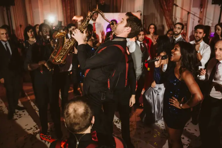 Saxophonist playing among dancing guests as a singer performs at an evening reception