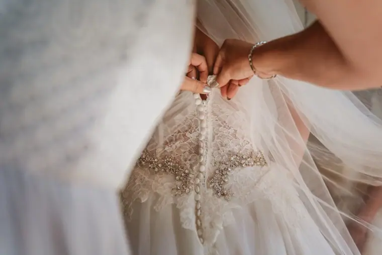 Close-up of buttons being fastened down the back of a beaded wedding gown