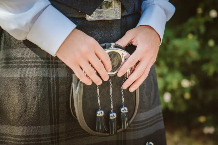 Close-up of hands holding a silver-trimmed sporran against a tartan kilt