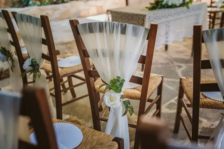 Wooden chairs with white tulle bows and greenery lining the ceremony aisle