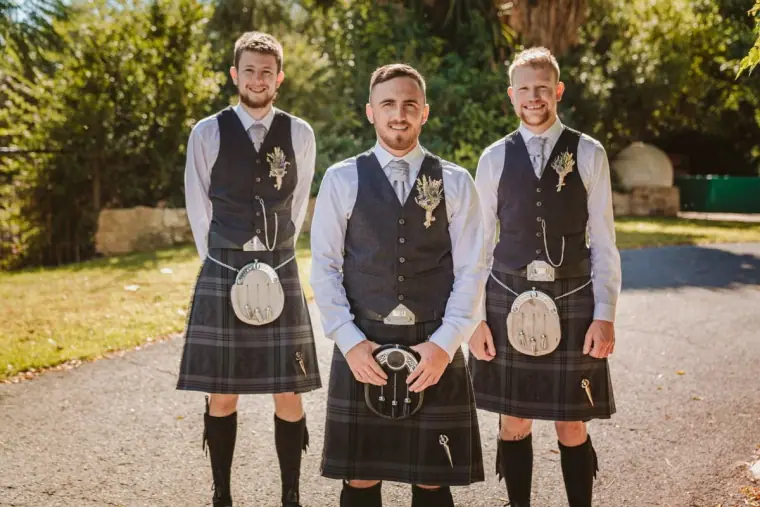 Groom and two groomsmen in matching tartan kilts and waistcoats smiling