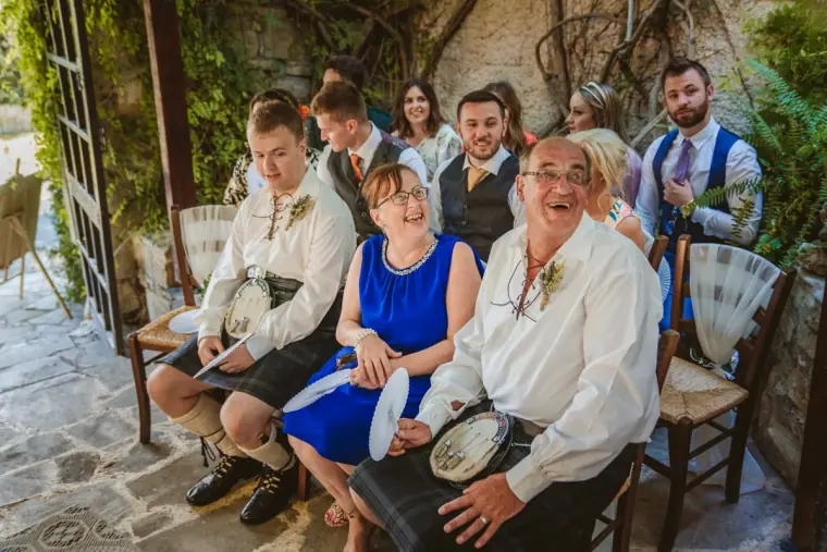 Seated guests in kilts and summer outfits laughing before the ceremony
