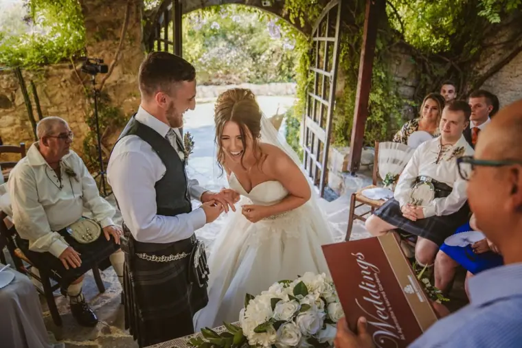 Hannah laughing during the ring exchange as guests in kilts look on