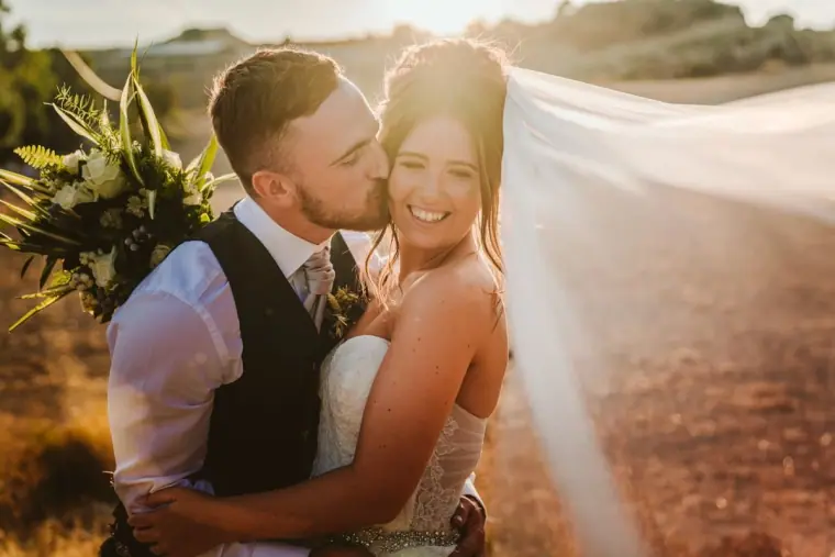 Keith kissing Hannah's cheek as her veil streams out in golden light