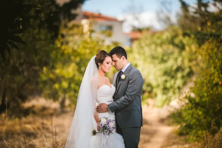 Groom in a grey suit holding his bride close on a garden path at a villa in Paphos