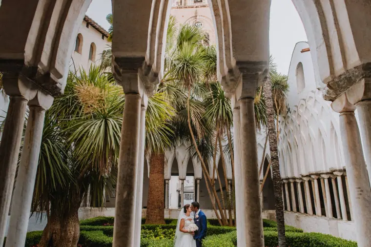 Couple standing in a palm-filled cloister of white arches on the Amalfi Coast