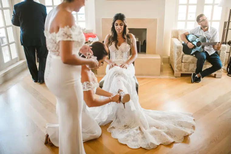 Bride being helped into her gown as a guitarist plays in the bridal suite at Anassa