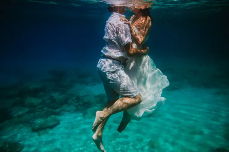 Underwater shot of a couple kissing in clear turquoise water, her dress floating