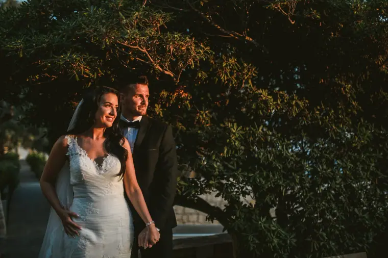 Jaclyn and Steven standing beneath dark trees in warm evening light at Almyra, Paphos