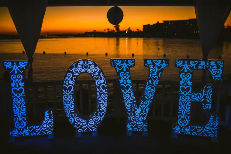 Illuminated blue LOVE letters in front of a sunset over the sea, Nissi Beach Resort