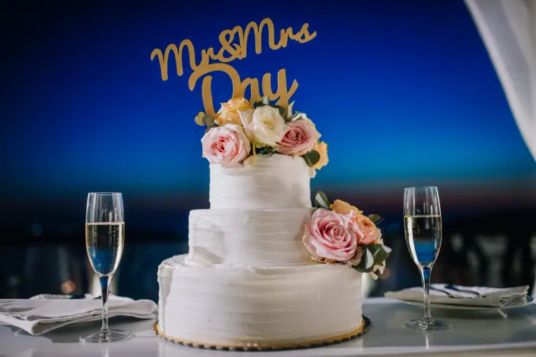 Three-tier white cake with roses and a gold "Mr & Mrs Day" topper at dusk in Santorini