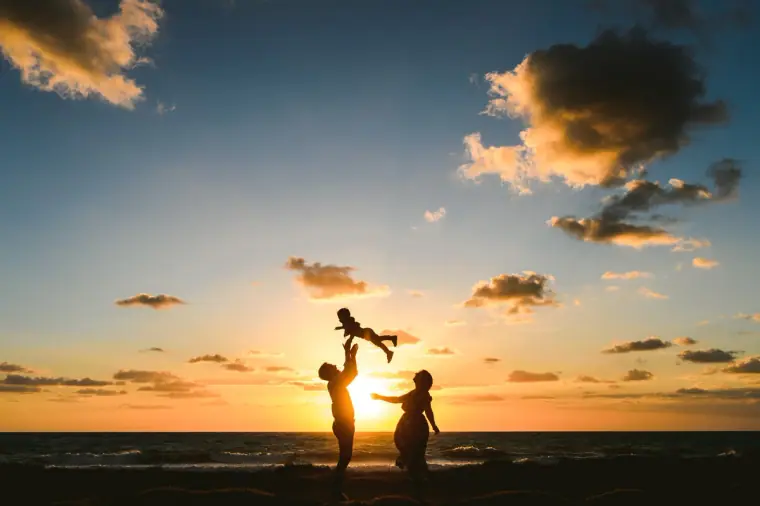 Silhouetted couple lifting a child into the air against a sunset over the sea, Paphos