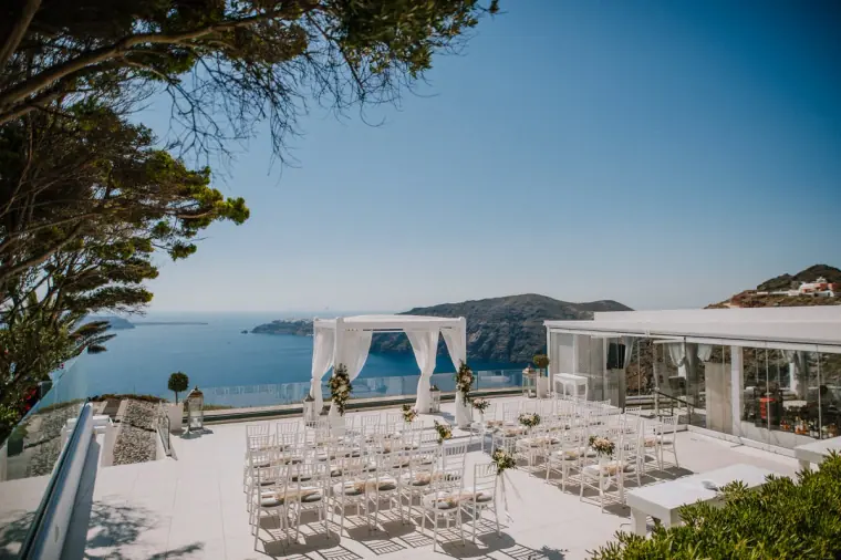 Clifftop ceremony set-up with white chairs and draped canopy overlooking the sea in Santorini