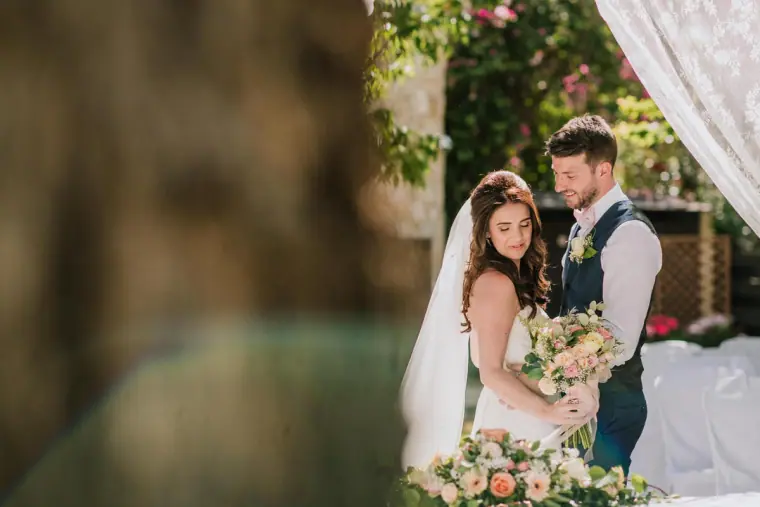 Bride and groom with her bouquet beside a white draped canopy, Vasilias Nikoklis Inn
