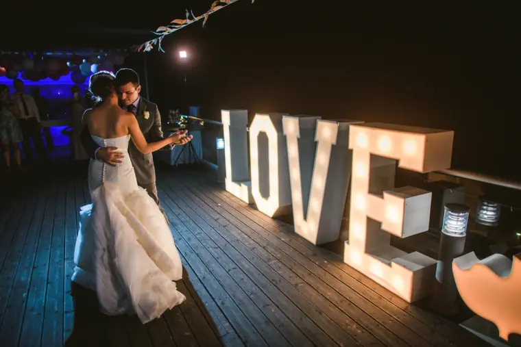Couple dancing beside glowing LOVE marquee letters on a deck at night at a villa in Paphos