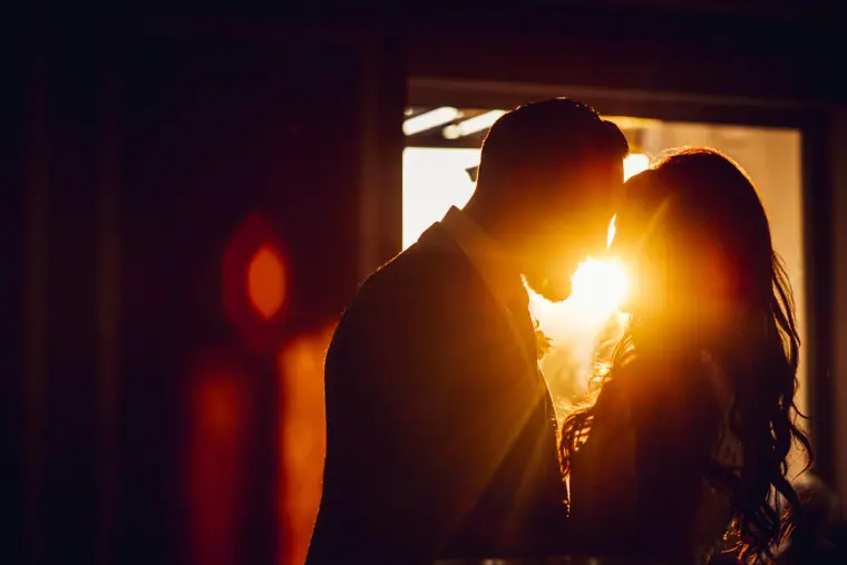 Silhouette of a couple kissing in a doorway with the sun glowing between them, Anassa