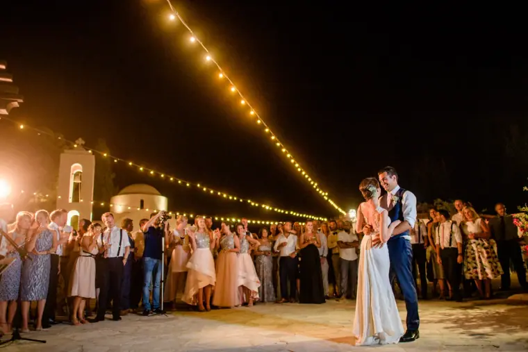 Kat and George's first dance under strings of festoon lights, guests circling, Anassa