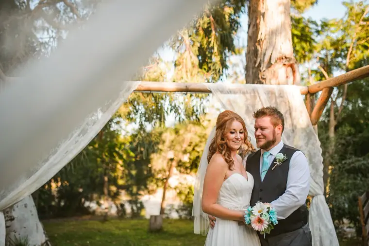 Vicky and Ian smiling beside a white draped ceremony arch, Vasilias Nikoklis Inn