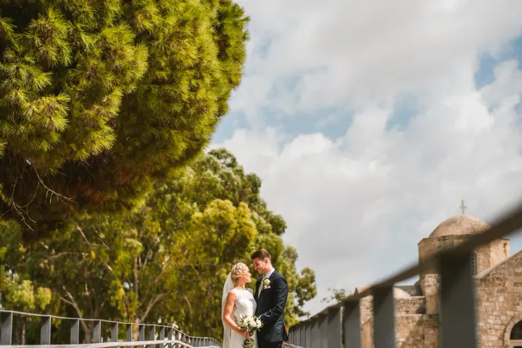 Rachel and Chris walking by a stone wall beneath tall pine trees, Pissouri