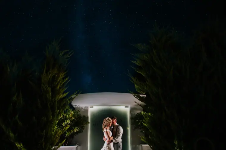 Couple embracing in a softly lit white gazebo under a starry night sky, Santorini