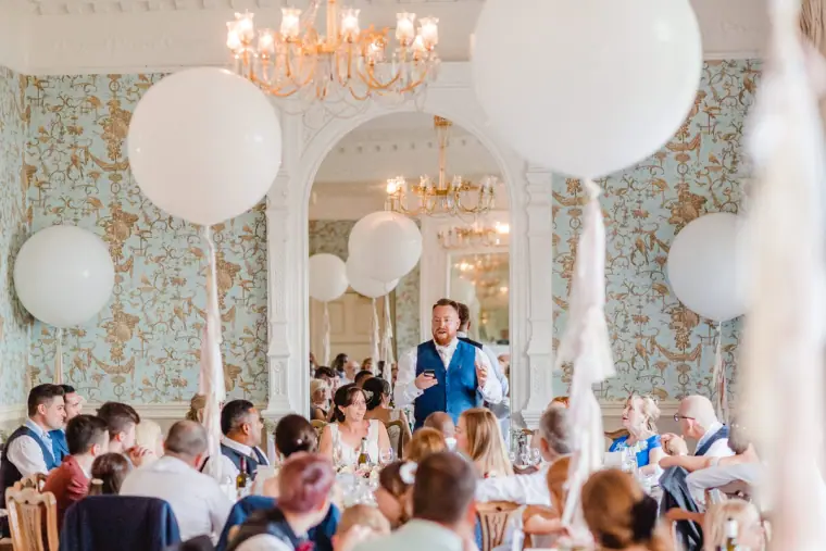 Guests listening to speeches in a chandeliered room with giant white balloons, Pendley Manor