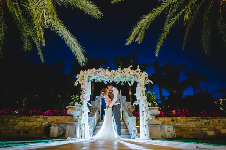 Couple kissing beneath a floral arch under palm trees at night, Olympic Lagoon, Ayia Napa