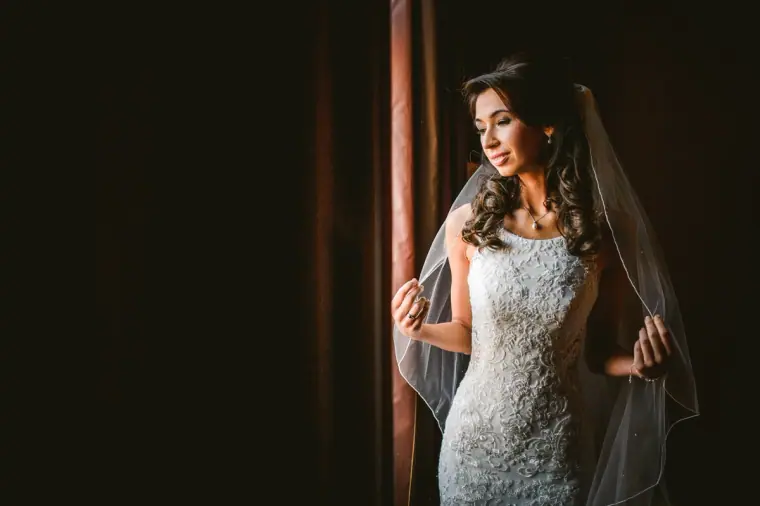 Elina in a lace gown and veil standing by a dark curtain at Wotton House, Surrey