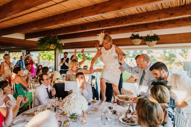 Guest standing on a chair at a lively lunch reception under a timber roof, Can Curreu, Ibiza