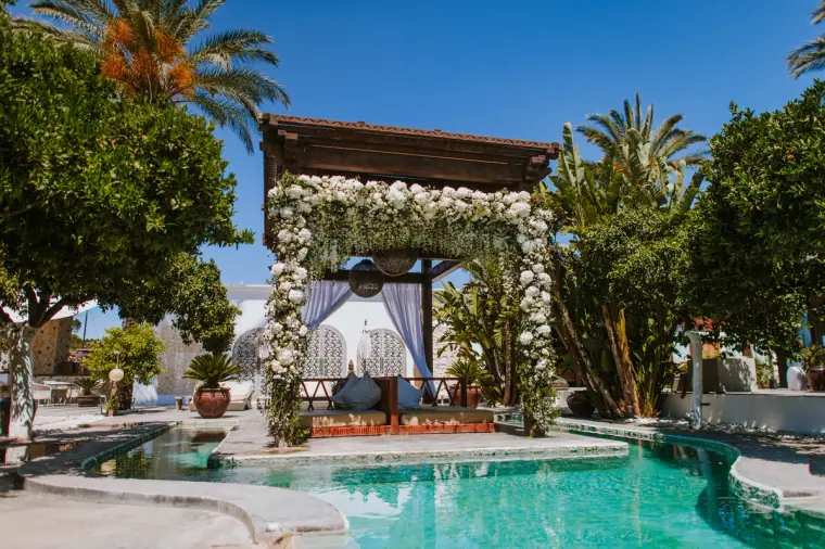 Floral-draped gazebo beside a turquoise pool among palm trees at an Ibiza venue