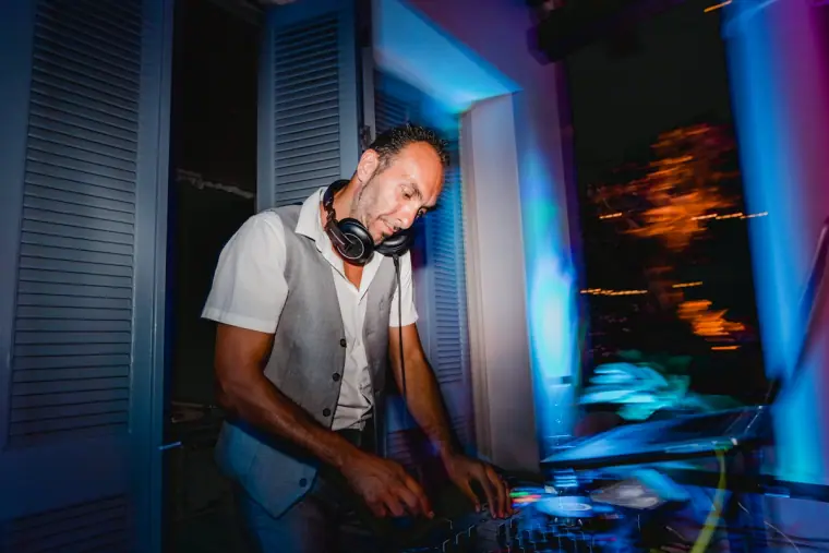 DJ in headphones mixing under blue and purple party lights, Anassa