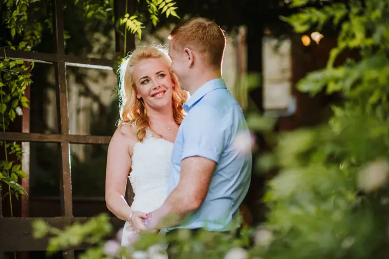 Smiling bride and groom in a light blue shirt among garden greenery, Vasilias Nikoklis Inn