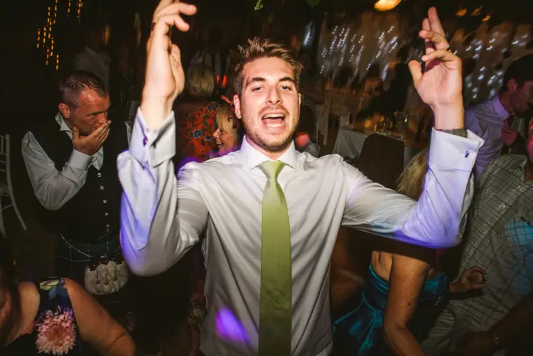 Groomsman in a green tie dancing with arms raised at the evening party, Pissouri