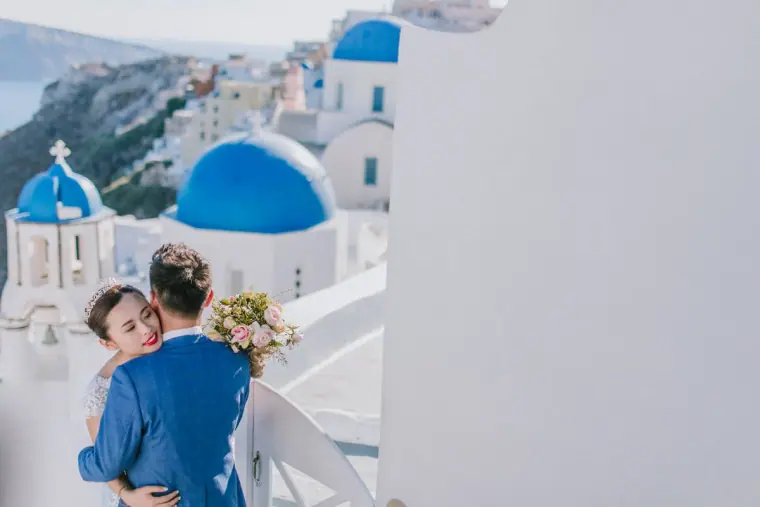 Couple hugging beside blue-domed churches and whitewashed buildings in Santorini