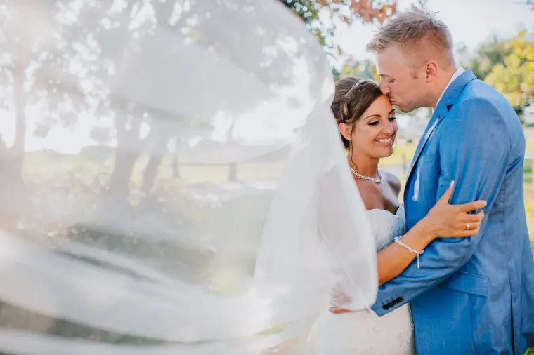 Grant in a blue suit kissing Terri's forehead behind her sheer veil, Aphrodite Hills