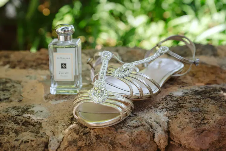 Silver strappy sandals beside a Jo Malone perfume bottle on a weathered stone