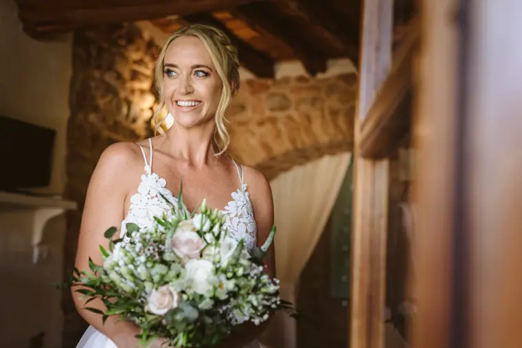Sophie beaming with a white and blush bouquet in a rustic stone room